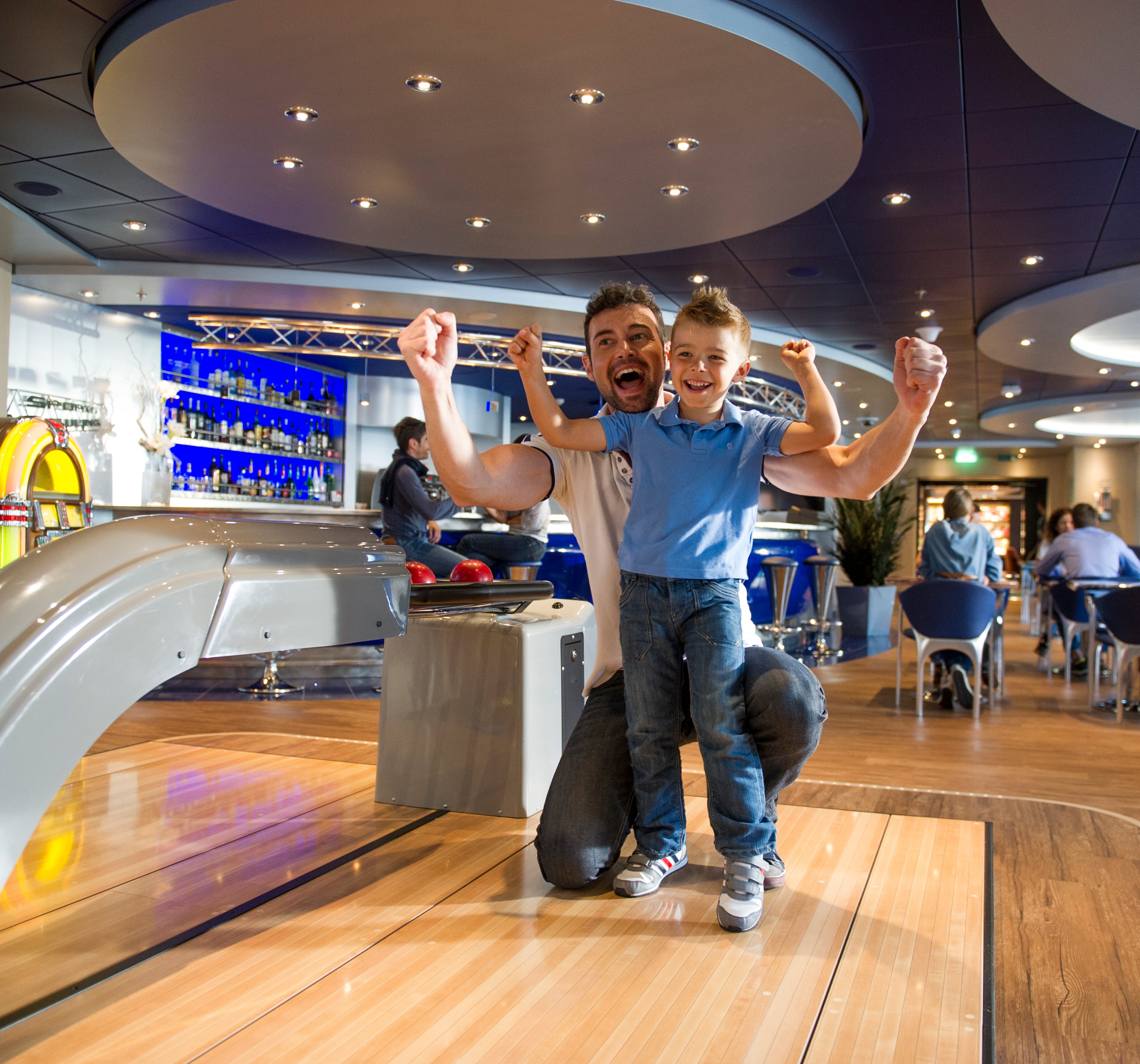 Father and son enjoying bowling onboard a cruise ship with a vibrant lounge in the background | MSC Cruises