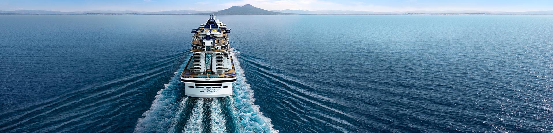 A luxury MSC cruise ship sailing towards a distant island | MSC Cruises A luxury MSC cruise ship sailing towards a distant island | MSC Cruises