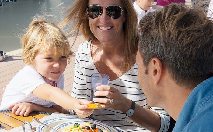 Family enjoying a meal on a sunlit cruise ship deck | MSC Cruises Family enjoying a meal on a sunlit cruise ship deck | MSC Cruises