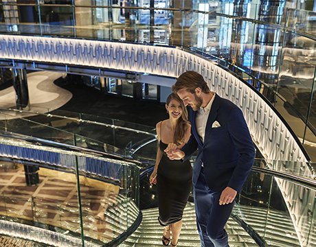 Elegantly dressed couple ascending a glass staircase aboard a luxurious cruise ship | MSC Cruises