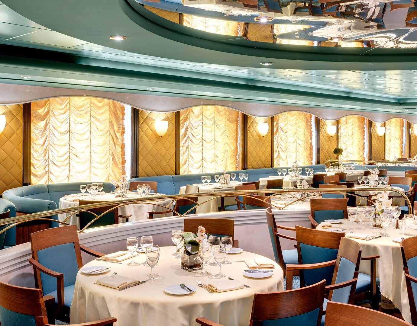 Elegant dining room with set tables and golden draped windows onboard a cruise ship | MSC Cruises Elegant dining room with set tables and golden draped windows onboard a cruise ship | MSC Cruises