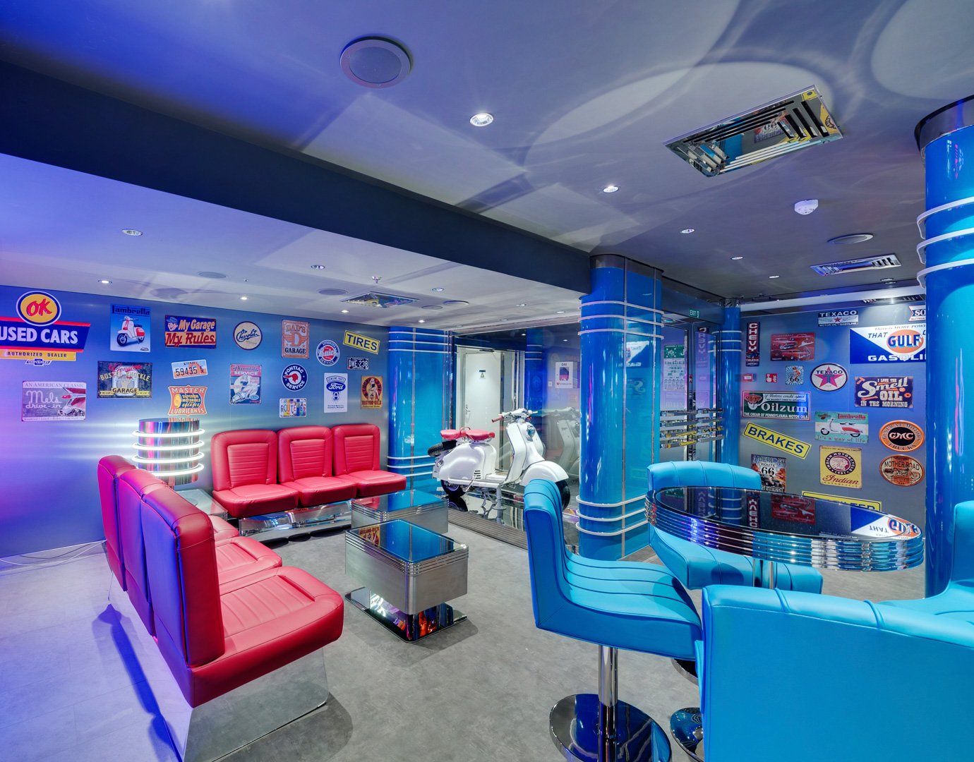 Retro-themed lounge with red and blue seating, vintage signs, and a white scooter on display | MSC Cruises Retro-themed lounge with red and blue seating, vintage signs, and a white scooter on display | MSC Cruises