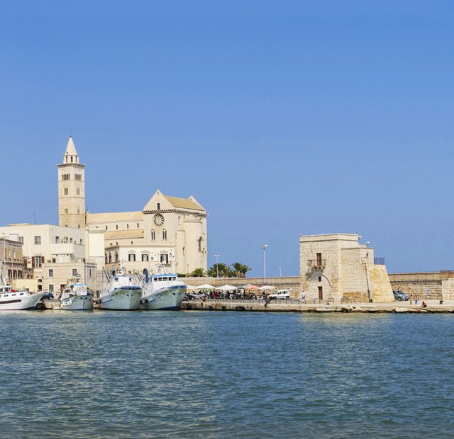Historic waterfront with Trani Cathedral and docked boats under a clear blue sky | MSC Cruises
