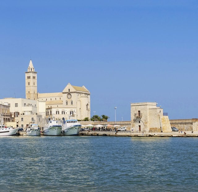 Historic waterfront with Trani Cathedral and docked boats under a clear blue sky | MSC Cruises Historic waterfront with Trani Cathedral and docked boats under a clear blue sky | MSC Cruises